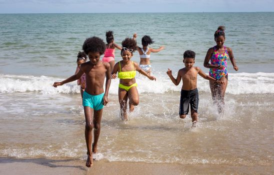 Kids playing running on sand at the beach, A group of children holding hands in a row on the beach in summer, rear view against sea and blue sky