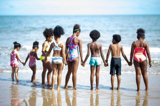 Kids playing running on sand at the beach, A group of children holding hands in a row on the beach in summer, rear view against sea and blue sky