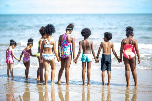 Kids playing running on sand at the beach, A group of children holding hands in a row on the beach in summer, rear view against sea and blue sky