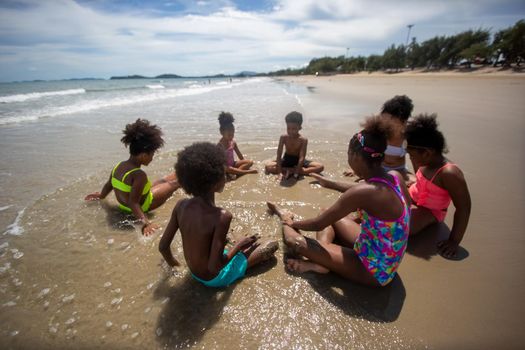 Kids playing running on sand at the beach, A group of children holding hands in a row on the beach in summer, rear view against sea and blue sky