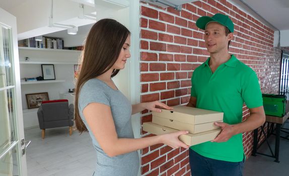 Young man delivering food to customer at doorway, Paper pocket and food containers in hands of a smiling deliveryman outdoors. Quality service of a restaurant.