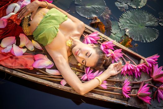 Young Asian women in Traditional dress in the boat and pink lotus flowers in the pond.Beautiful girls in traditional costume.Thai girl in retro Thai dress, Thai girl in traditional dress costume
