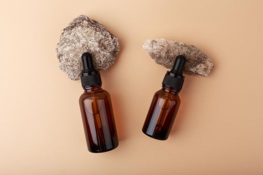 Top view of two dark brown cosmetic bottles with black cap on stones at simple beige background. Concept of anti aging, moisturizing and collagen boosting skin care 