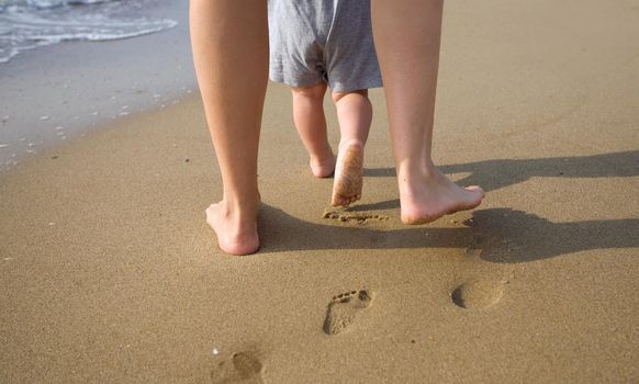 mom helps to make the child's first steps on the beach