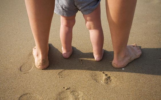 mom helps to make the child's first steps on the beach