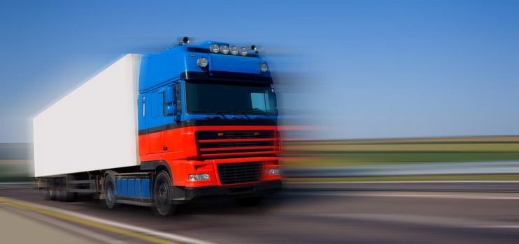 Red blue truck on blurry asphalt road 