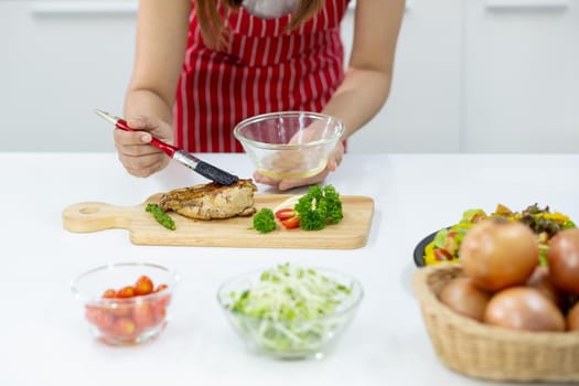 Close up hands of woman smear oil on piece of fish or meat on wood plate on white table with other food ingredients.