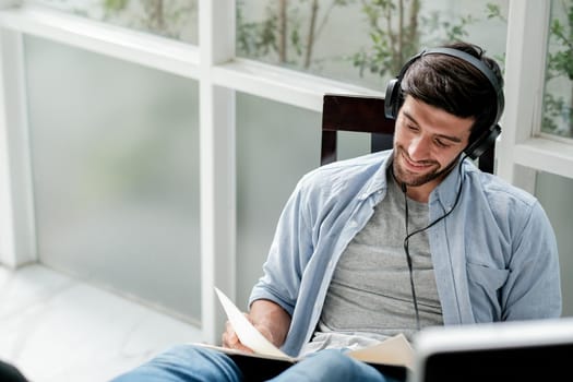 Soft blurred of Caucasian man read book and listen music by headphone with relax and happy expression in room with day light.