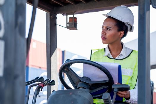 African American foreman woman or cargo container worker sit on cargo car and look to left side also thinking action during working. Industrial support system help employee performance concept.
