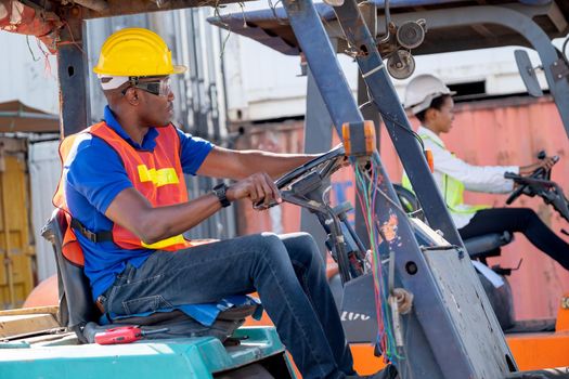 African American foreman or cargo container worker drive cargo car and look at his co-worker woman also drive in workplace area. Industrial support system help employee performance concept.