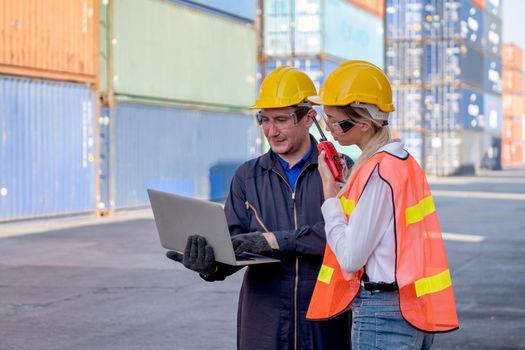 Concept of industrial support work system. Two foreman and cargo container worker discuss together in workplace area with one hold and using laptop and the other hold walkie-talkie to contact team.