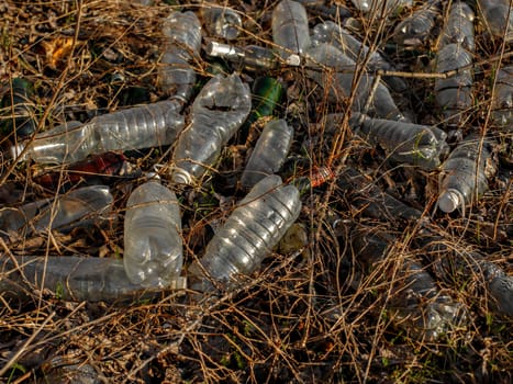 Pile of plastic and glass bottles in dry grass. Environmental pollution.