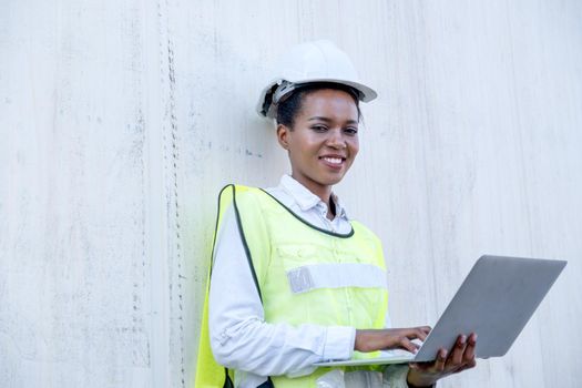 African American foreman woman hold laptop and lean on white cargo container also smile with look at camera in shipping area.