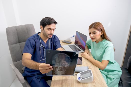 Beautiful Asian woman discuss with doctor who hold x-ray film and explain the information of process of treatment the patient in clinic room.