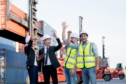 Cargo container workers or group of employee express happy emotion and action look lite celebrate with successful of work in workplace area with crane and shipping container stack as background.