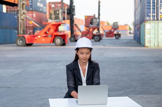 Asian cargo container worker of engineer woman use laptop in workplace area with concept of quality control for industrial business.