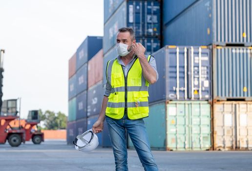 Factory of cargo container worker man take of mask and hardhat after finish work. Concept of new normal lifestyle in industrial business during pandemic of Covid-19 coronavirus in city.