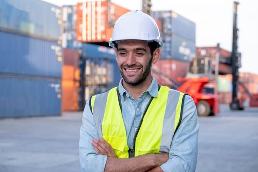 Portrait of engineer worker of factory technician stand with happy emotion and in front of cargo container crane in workplace area. Concept of good support best successful for industrial business.