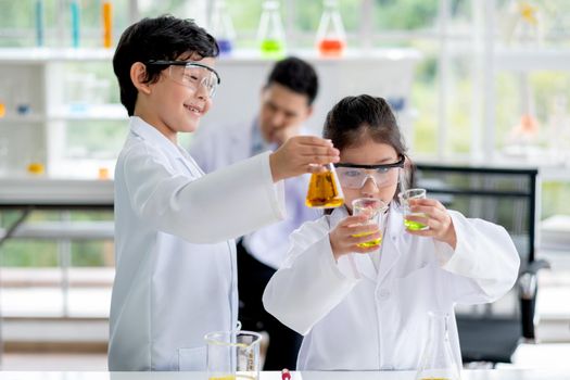 Little boy and girl scientist enjoy to examine the color chemical in laboratory by girl compare color of chemical. Concept of good practice and education of science for children support.