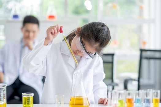 Lovely little girl scientist enjoy and concentrate to examine the color chemical in laboratory by using dropper with day light. Concept of good practice and education of science for children support.