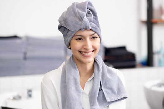Portrait of beautiful Caucasian woman with towel to cover her head and hair is smiling look to the right side and stay in beauty salon shop.