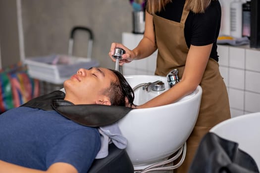 Close up hands inject water to wash Asian man hair after finish process of haircare in beauty salon shop.