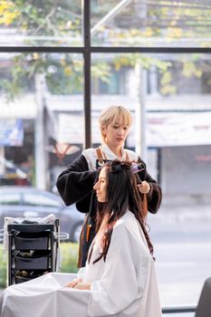 Asian beauty salon barber girl work with hair style of beautiful Caucasian girl sit in the shop. Beauty business for good appearance of people concept.
