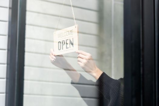 Close up hands hold banner of word, open, in front the shop to notice and invite people to go inside and get service.