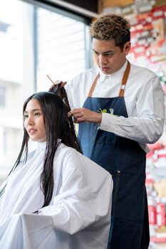 Asian beautiful customer woman sit and is processed of hairstyle by beauty salon barber man. Concept of beauty business for good looking for people.