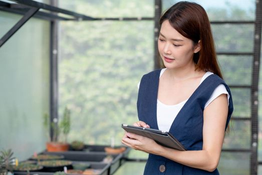 Close up portrait beautiful Asian woman hold tablet to check quality and physical of plant product in her green house. Sustainable with business work involve with plant of flora concept.