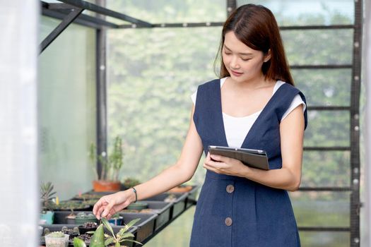 Beautiful Asian girl hold tablet to check quality and physical of plant product in her green garden of her house. Sustainable with business work involve with plant of flora concept.
