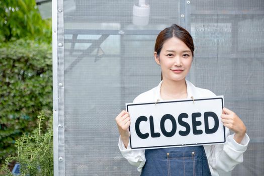 Beautiful Asian woman present banner with word closed in front of green house and sad emotion relate with close the business of sustainable activity.