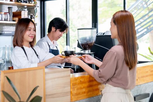 Beautiful Asian woman receive plate with coffee from barista or woman worker in coffee shop. Concept of small business and support by customer.