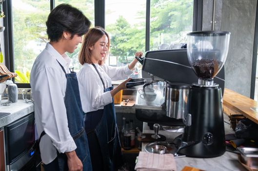 Barista man stand near his co-worker who prepare of produce coffee using the coffee maker machine and they look happy by smiling for working together.