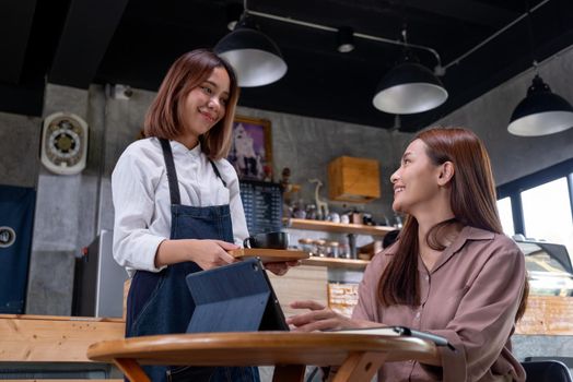 Beautiful working woman sit in coffee shop and get service from barista woman and they smile to each other with happy emotion.