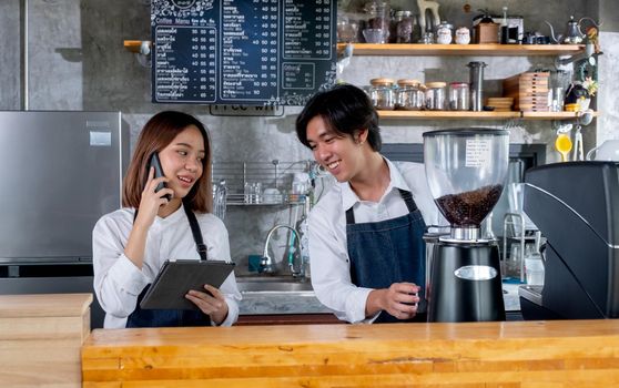 Barista woman or coffee maker answer the phone to get order from customer while her co-worker prepare and produce coffee and they are work as good teamwork with small business.