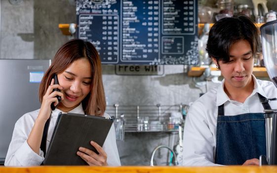 Barista woman or coffee maker answer the phone to get order from customer while her co-worker prepare and produce coffee and they are work as good teamwork with small business.