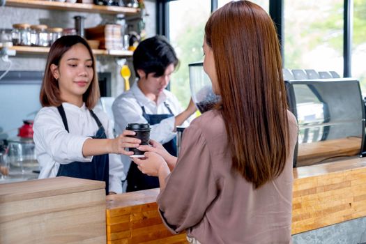 Barista girl or coffee maker give cup of coffee to her customer woman in coffee shop. Happy working with small business and sustainable concept.