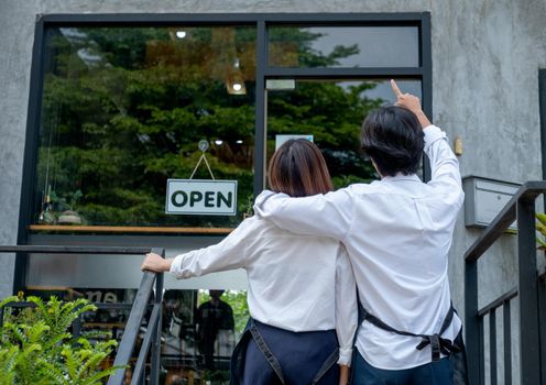 Back of couple coffee makers or coffee shop staffs that man point to the building and talk to woman. Concept of good teamwork support small business system.