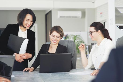 Three young successful business women in the office, together, happily working on a project. 