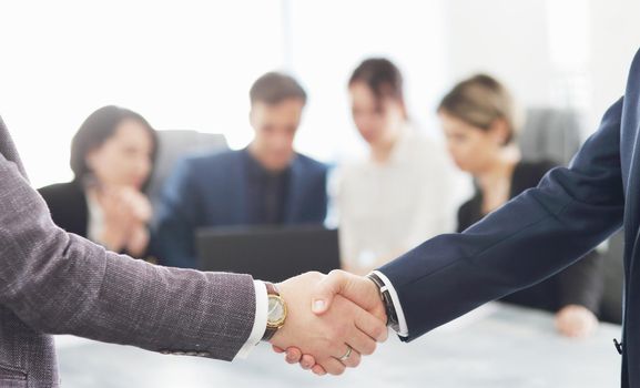 Business people shaking hands finishing a meeting in the background of their work team. 