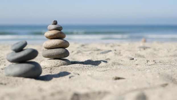 Rock balancing on ocean beach, stones stacking by sea water waves. Pyramid of pebbles on sandy shore. Stable pile or heap in soft focus with bokeh, close up. Zen balance, minimalism, harmony and peace