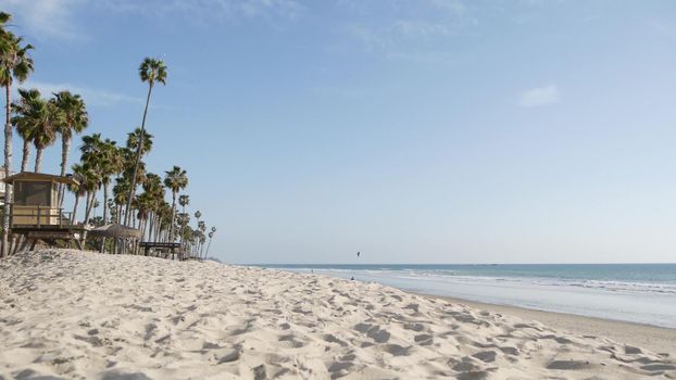 Tropical palm trees, white sandy beach by sea water wave, pacific ocean coast, San Clemente California USA. Blue sky and lifeguard tower. Life guard watchtower hut, summertime shore. Los Angeles vibes