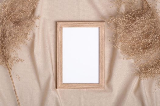 Picture frame with blank paper card mockup near to pampas dry grass on beige neutral colored textile