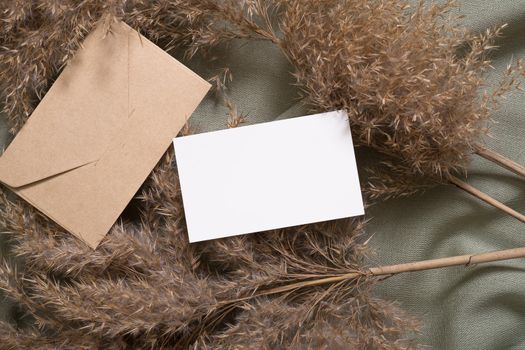 White blank paper card and envelope mockup with pampas dry grass on green neutral colored textile