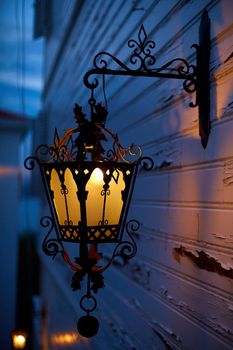 Glowing old street lamp lighting on the facade of the house. Twilight on the street of the old city.