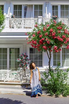 A charming brunette girl walks along the street of Buyukada island in Turkey. Summer sunny day and blossoming trees.