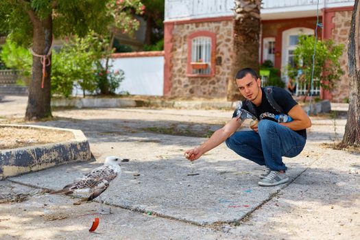 The guy feeds the seagulls with bread on the embankment.