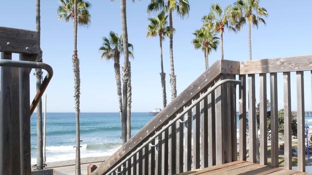 Wooden stairs, beach access in Oceanside, California USA. Coastal stairway, pacific ocean waves and palm trees. Vacations by sea in United States. Sunny tropical day, summertime aesthetic. Staircase.