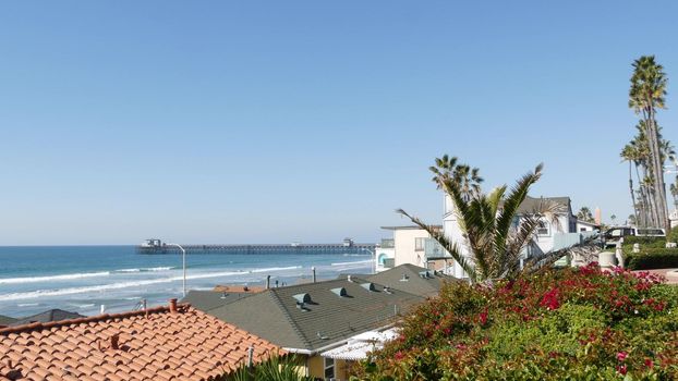 Pacific ocean beach, green palm trees and pier. Sunny day, tropical waterfront resort. Vista viewpoint in Oceanside, near Los Angeles California USA. Summer sea coast aesthetic, seascape and blue sky.